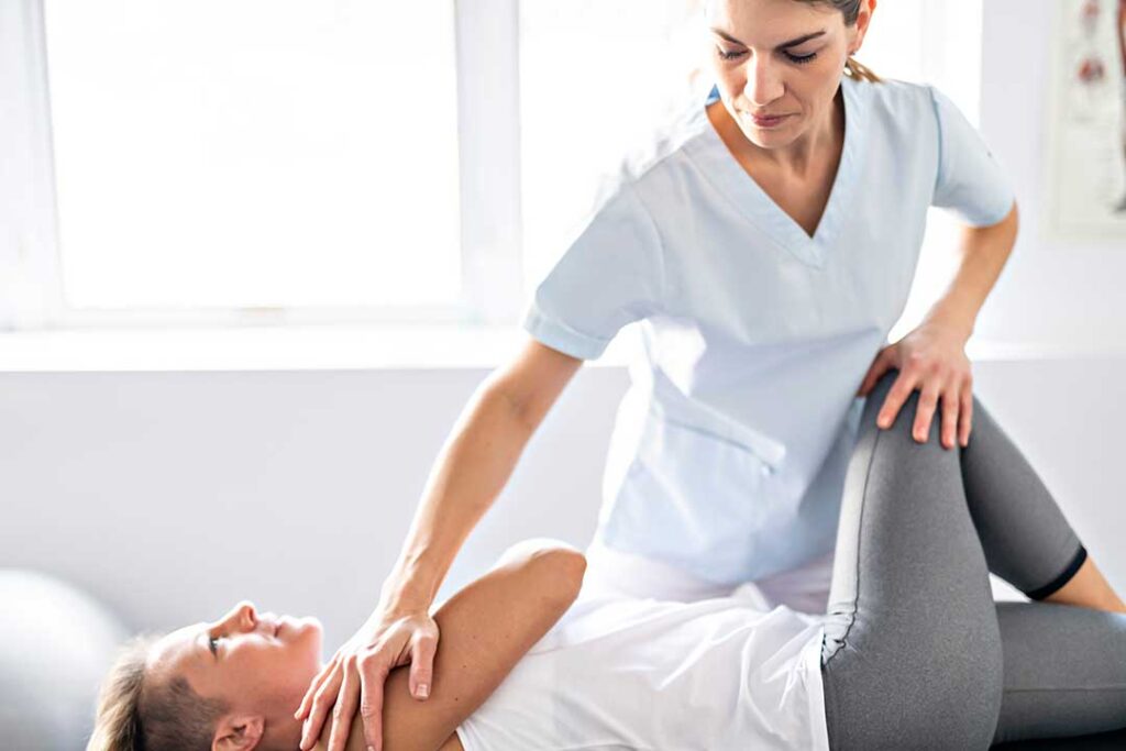A close-up of a person's hand massaging a sore spot on their shoulder while seated indoors.